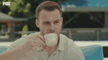 a man is drinking a cup of coffee with the fox logo in the corner