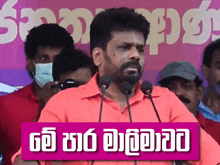 a man wearing a red shirt is speaking into microphones in front of a sign that says ' sinhala '