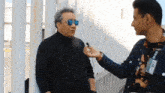 a man wearing sunglasses is being interviewed by a man wearing a name tag that says ' alonso '