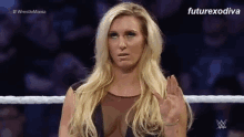 a woman in a black dress is standing in a wrestling ring giving the middle finger .
