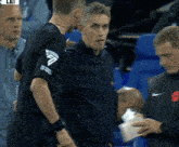 a man wearing a black shirt with the letter f on the sleeve talks to another man