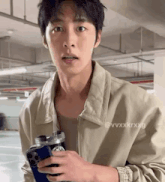 a man in a tan jacket is holding a cell phone and a water bottle .