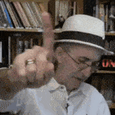 a man wearing a hat and glasses is giving the middle finger in a library .