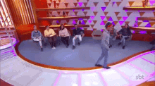 a group of people are sitting on a couch in a room while a man is walking on a stage .
