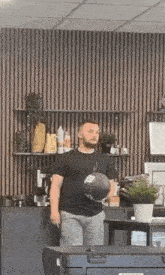 a man in a black shirt is standing in a room holding a helmet .