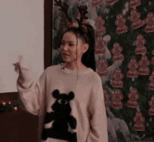 a woman wearing a sweater with a teddy bear on it is standing in front of a gingerbread man wallpaper .