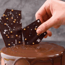 a person holds a piece of chocolate over a chocolate cake