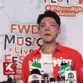 a man wearing glasses and a red shirt is standing in front of microphones .