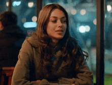 a woman in a green sweatshirt sits in front of a window at night