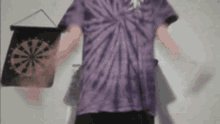 a man in a purple tie dye shirt is holding a dart board in his hand .