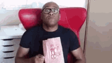 a man is sitting in a red chair eating popcorn .