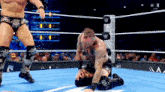 a wrestler is kneeling down in a wrestling ring while another wrestler stands in the corner
