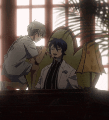 a man in a white coat sits in a chair while another man stands next to him