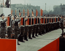 a group of soldiers are marching in a line with flags in the background