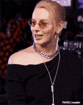 a woman wearing glasses and a chain necklace is smiling .