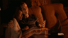 a man and a woman are sitting on a couch with the bet logo in the corner