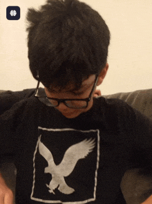 a boy wearing glasses and a black shirt with a white eagle on it