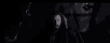 a man with a beard is sitting in a dark room with chains around him .