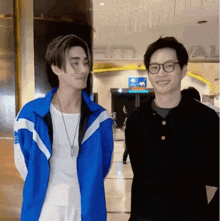 two young men are standing next to each other and smiling . one of the men is wearing glasses .