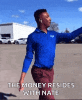 a man in a blue shirt and red pants is dancing in a parking lot with the words the money resides with nate below him