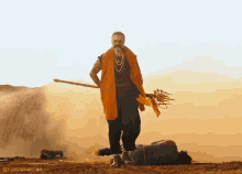 a man holding a spear in the desert with kandamure films written on the bottom right