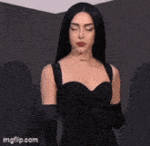 a woman in a black dress and black gloves is standing in front of a wall .