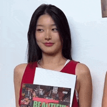 a woman in a red tank top is holding a magazine in her hand and smiling .