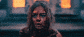 a woman with blood on her face is looking at the camera in front of a fire .