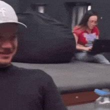 a man wearing a la hat is smiling with a woman in a red shirt in the background