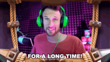 a man wearing green headphones says " for a long time " in front of a microphone