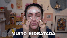 a woman with a lot of rings on her fingers is applying a cream to her face and says muito hidratada