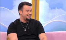 a man wearing a black shirt and a silver necklace is sitting on a pink couch
