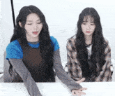two girls with long hair are sitting at a table with their hands outstretched