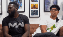 two men are sitting on a couch and one has a shirt that says mw