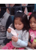 a little girl is holding a piece of paper in her hand while sitting next to another girl .