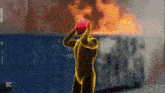 a man holding a red object in front of a burning building
