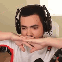 a man wearing headphones is covering his mouth with his hands while sitting in front of a microphone .