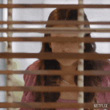 a woman is looking out of a window with blinds on .