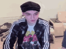 a young man wearing a black hat and a black adidas jacket is sitting in a chair .