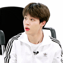 a young man wearing a white adidas jacket looks surprised