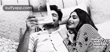 a man and a woman are sitting on a bed and looking at a book .