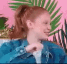 a woman with red hair is wearing a blue jacket and a ponytail while sitting on a couch .