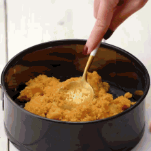 a person is using a gold spoon to stir something in a black pan