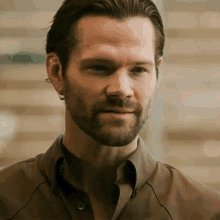 a close up of a man 's face with a beard wearing a brown shirt
