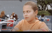 a young girl is sitting at a table in a restaurant looking at the camera