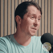 a man in a blue shirt is sitting in front of a microphone with a picture of a smiley face on it