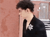 a man with curly hair is wearing a black jacket with a flower brooch on his collar .