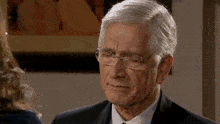a man wearing glasses and a suit is looking down