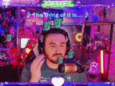 a man wearing headphones and a microphone is sitting in front of a screen that says the thing of it is .