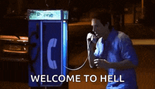 a man is talking on a payphone with the words welcome to hell written on the bottom .
